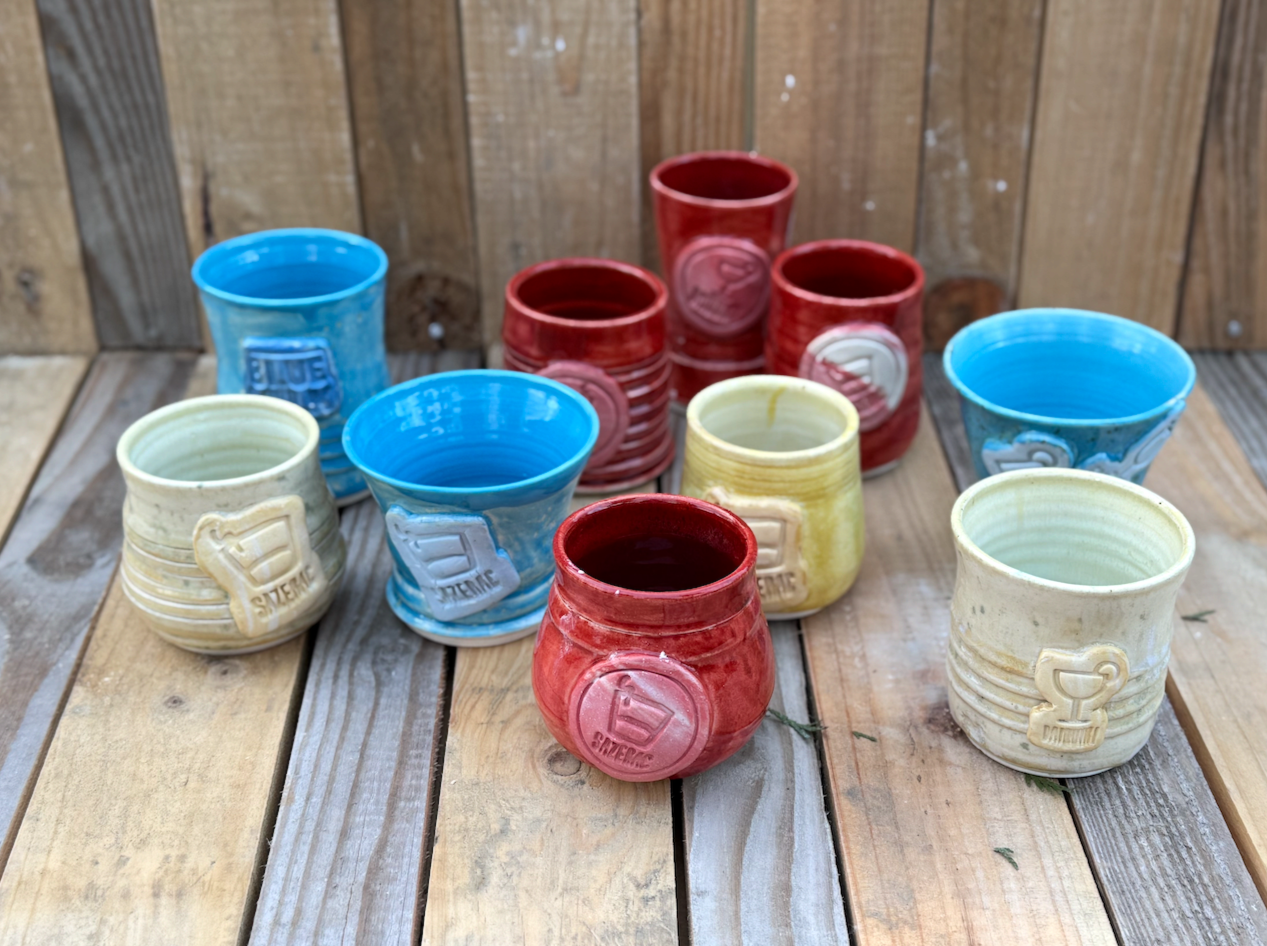 Colorful ceramic cups with embossed weights and handles, arranged on a wooden surface.