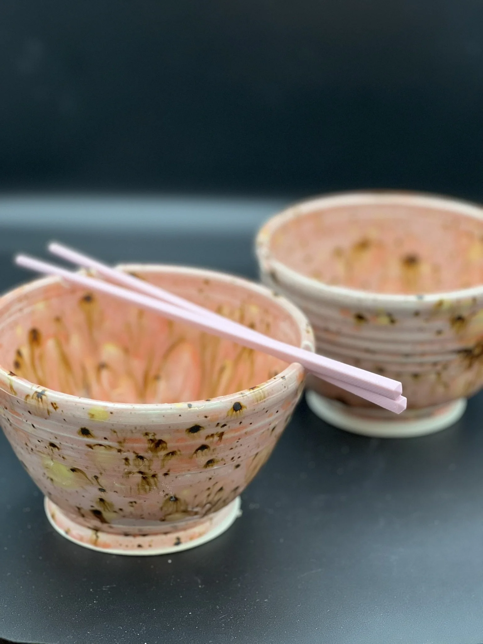 Two small bowls with pink chopsticks resting on one of them, placed on a dark surface.