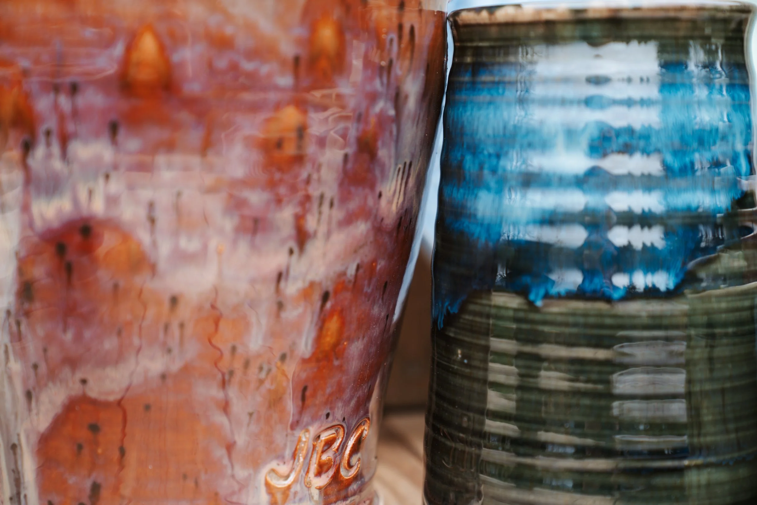 Close-up of two colorful, textured ceramic mugs, one with orange and red glaze, the other with blue and green glaze.