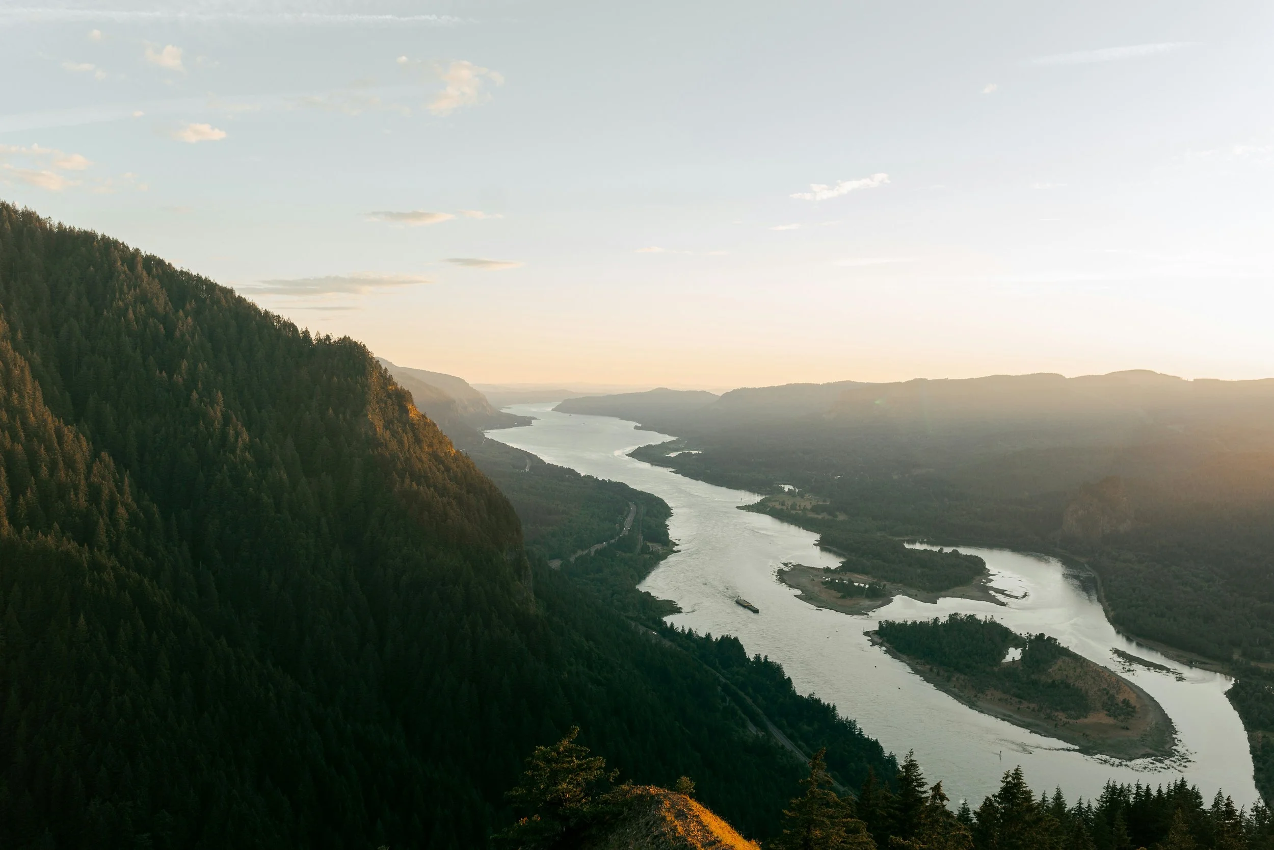 A river meandering through a lush green valley surrounded by forested mountains during sunset.