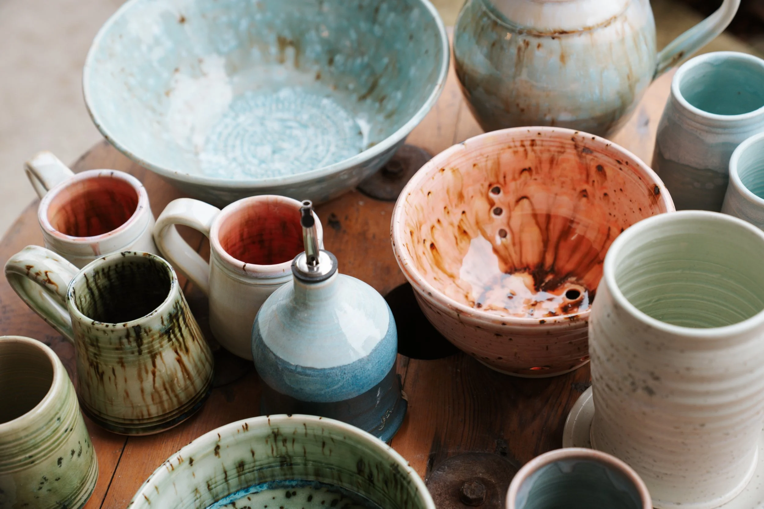 Collection of handcrafted ceramic bowls and mugs on a wooden table.