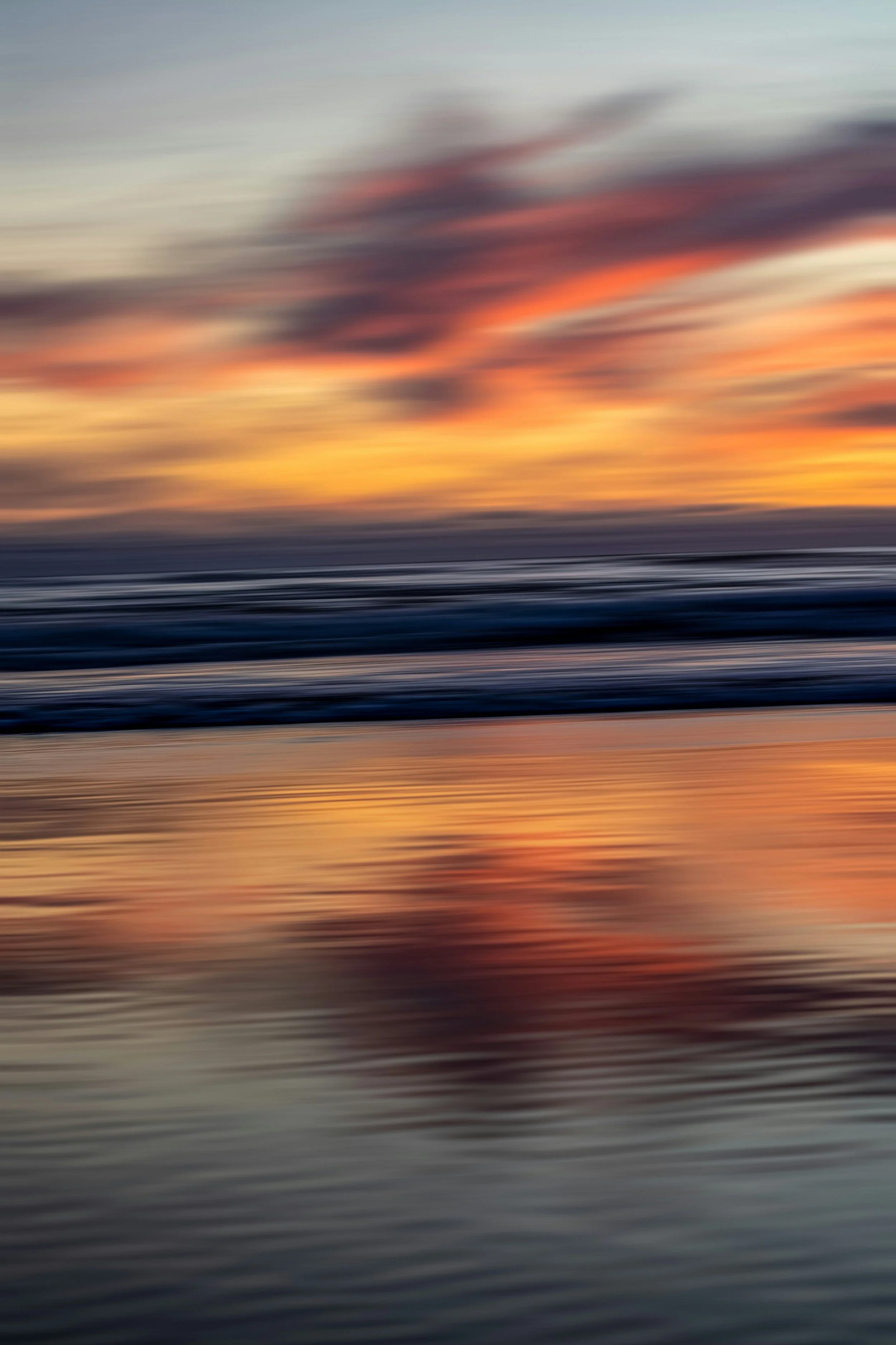 Blurred image of a sunset over the ocean with colorful clouds and reflections on the water.