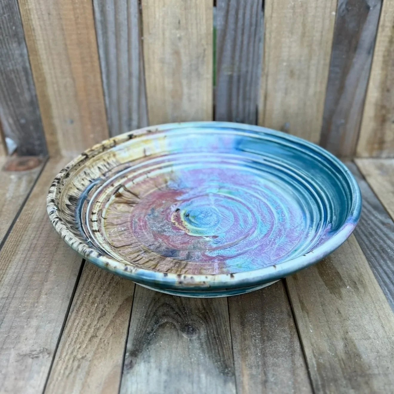 Colorful ceramic bowl with swirling patterns in shades of blue, pink, and beige, placed on a wooden surface.