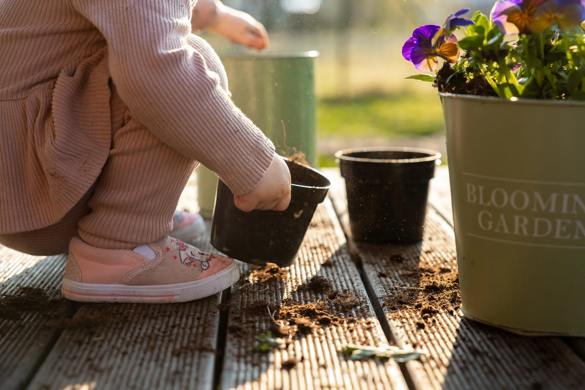A child in pink shoes and light clothing helping to plant pansies