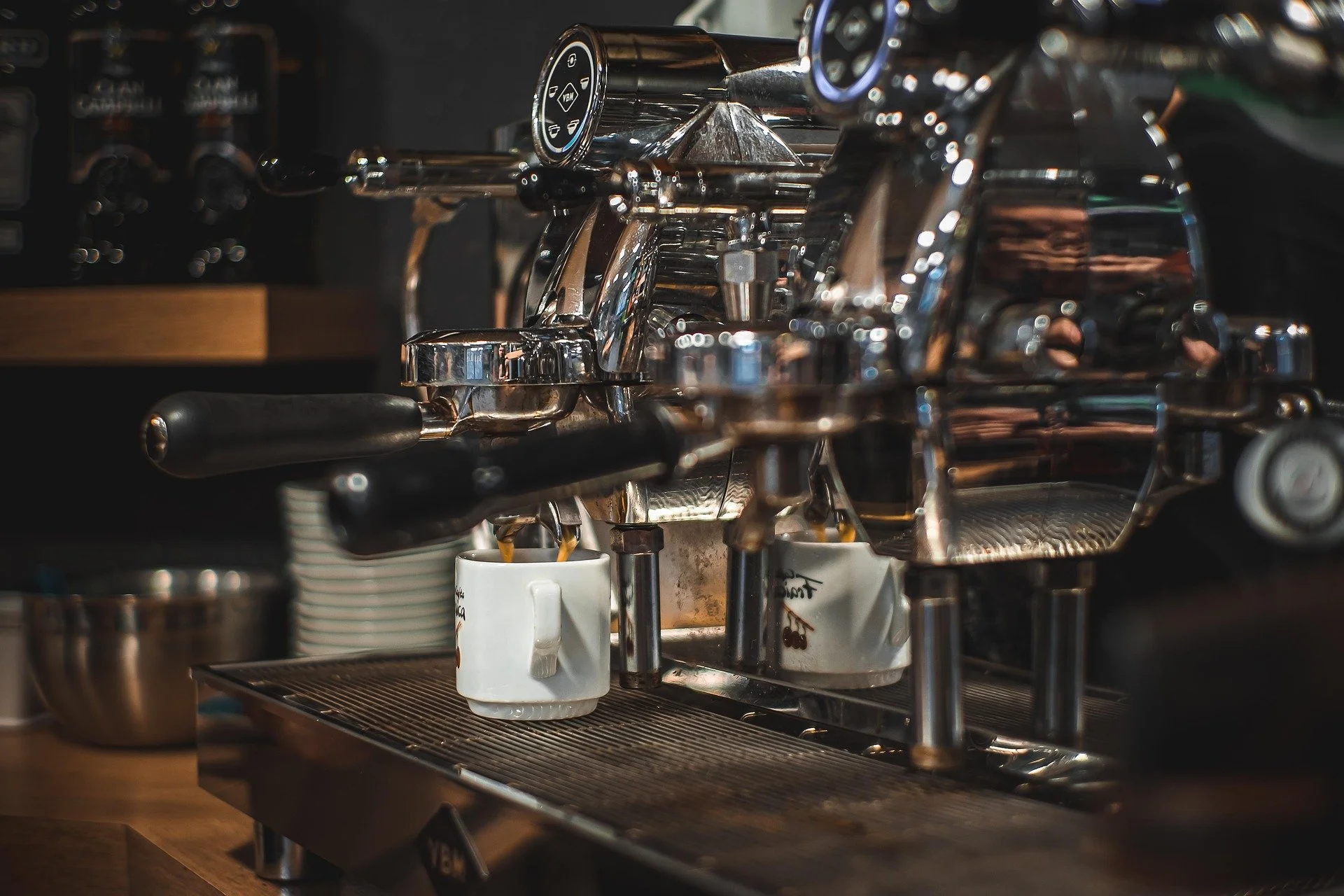Close-up of a shiny espresso machine with two cups underneath, in a coffee shop setting.