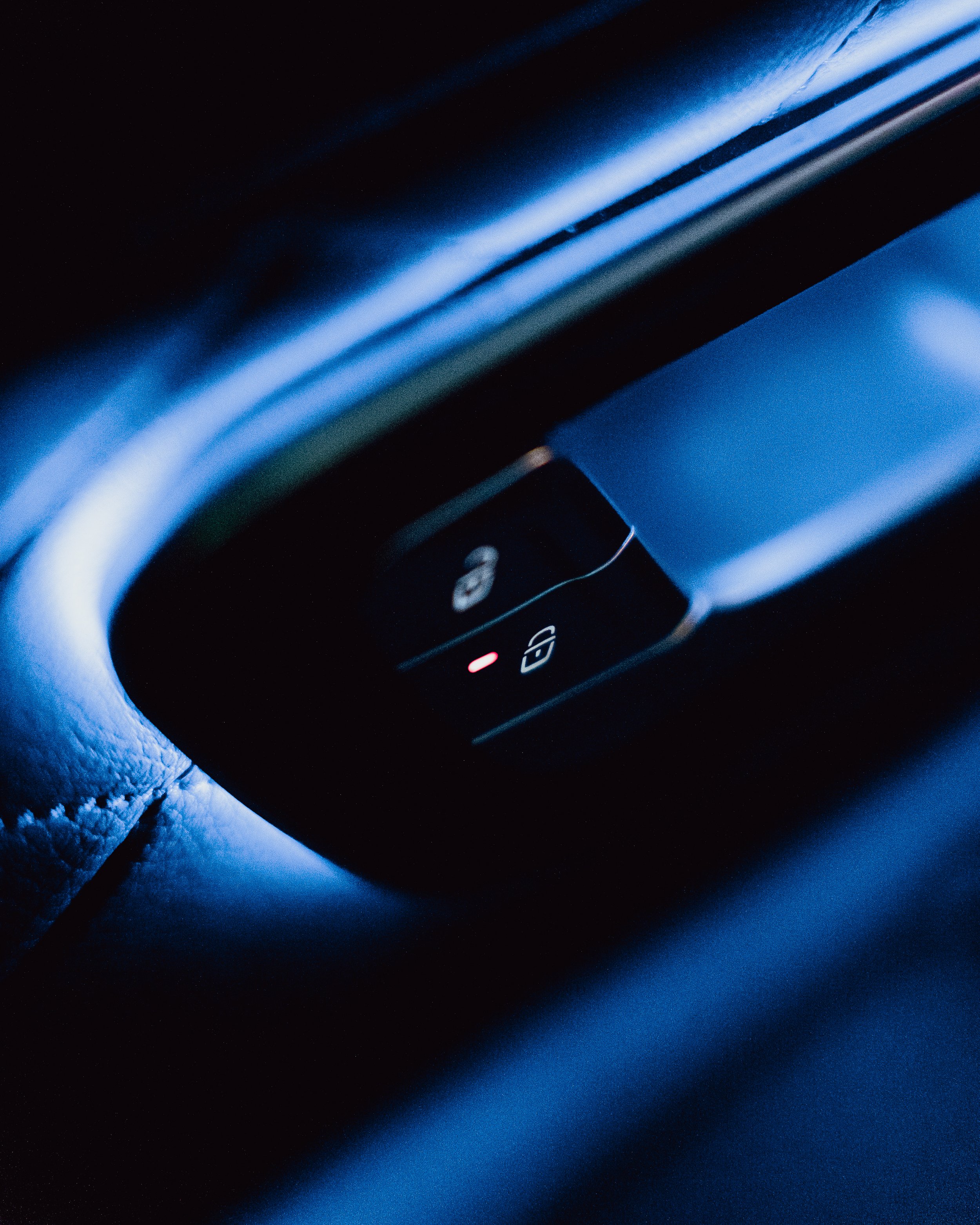 Close-up of car dashboard with illuminated lock and unlock buttons, illuminated by blue ambient lighting.
