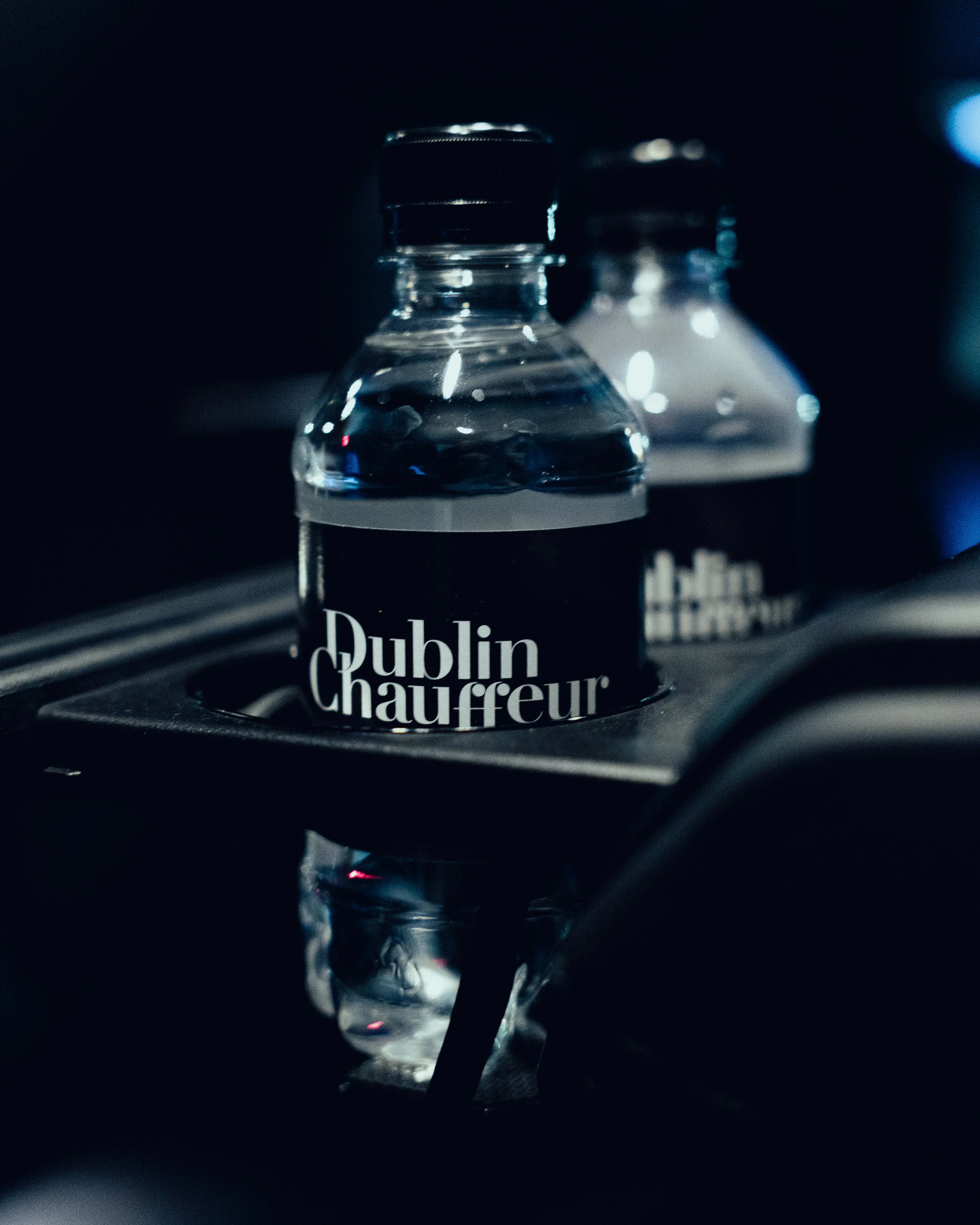 Close-up of two bottles of Dublin Chauffeur bottled water in a car's cup holder, with a dark background.