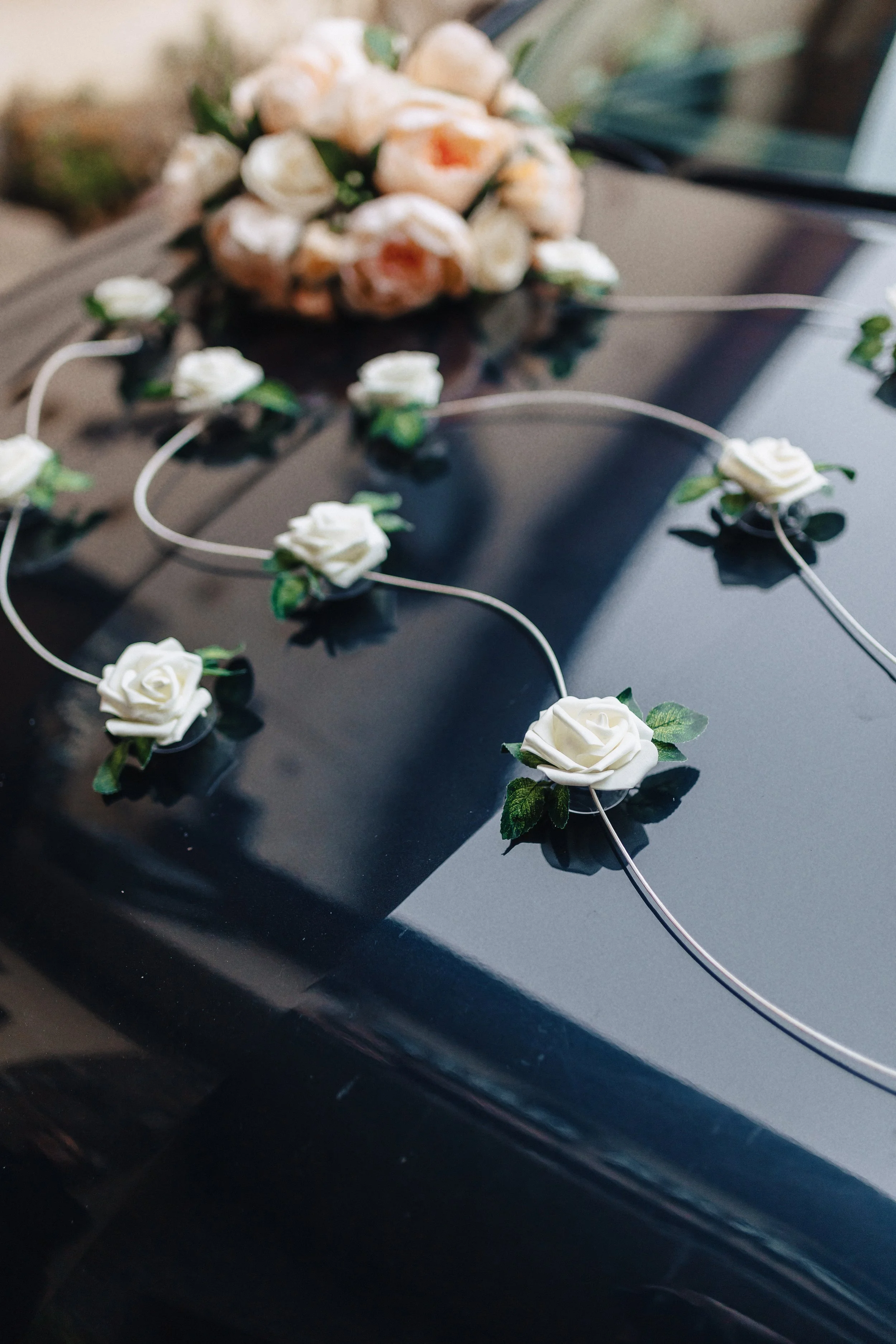 Decorative floral arrangement with white roses and green leaves on a black surface, possibly for a wedding or event.