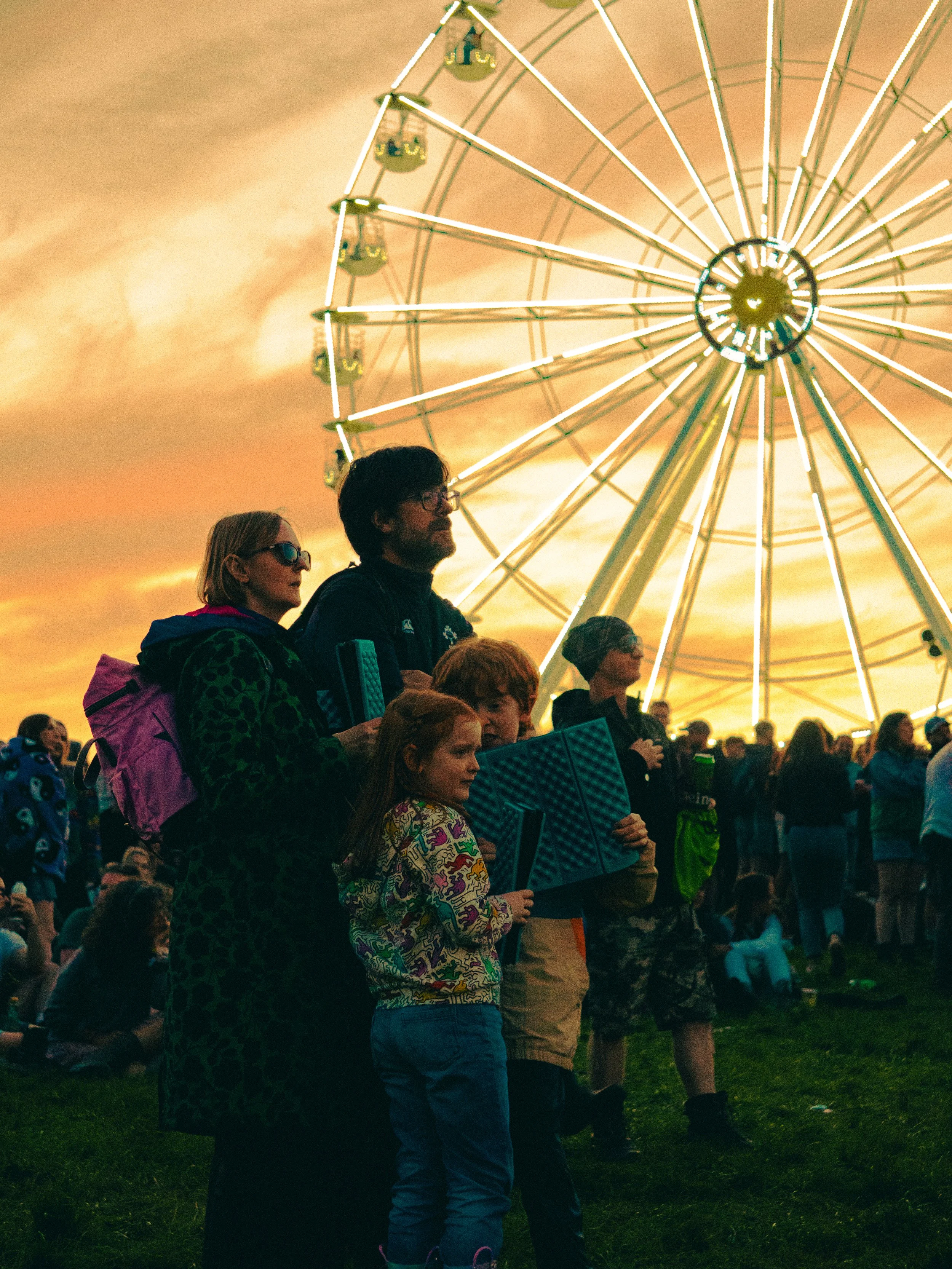 People watching a Ferris wheel at sunset with a colorful sky.