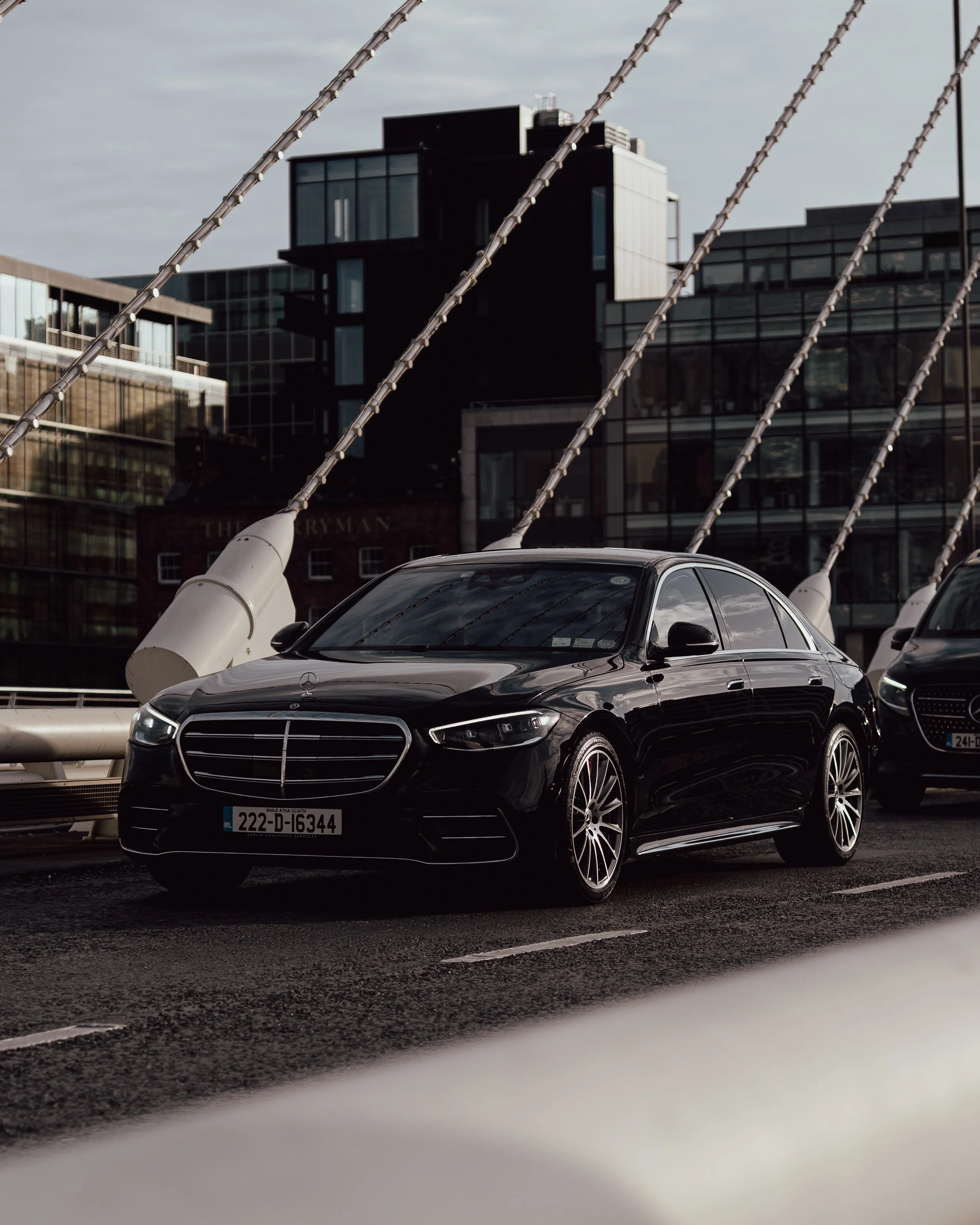 A black luxury Mercedes-Benz sedan parked on an urban street with modern glass buildings in the background.