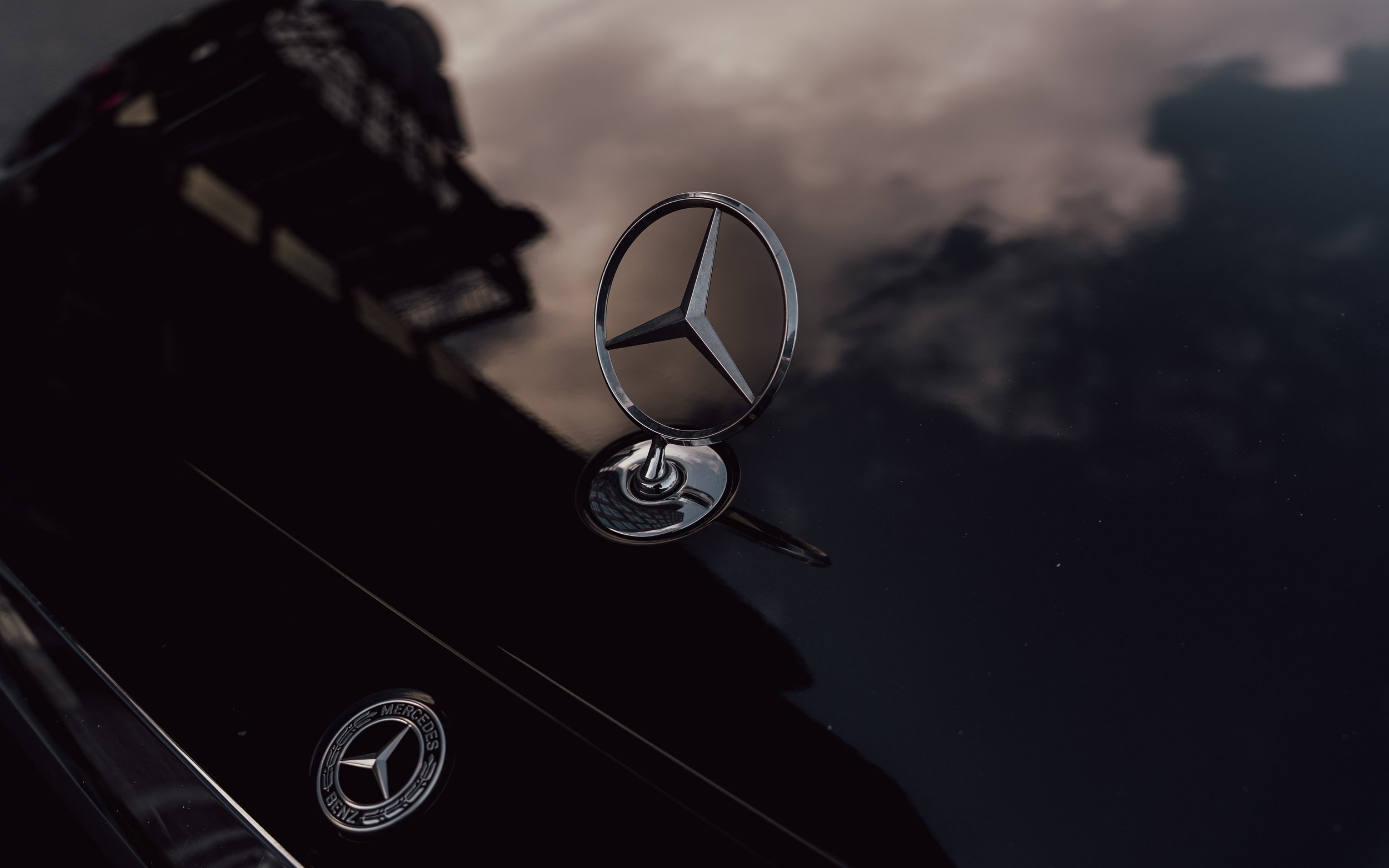 Close-up of a Mercedes-Benz emblem on a black car with a reflection of the sky and clouds.