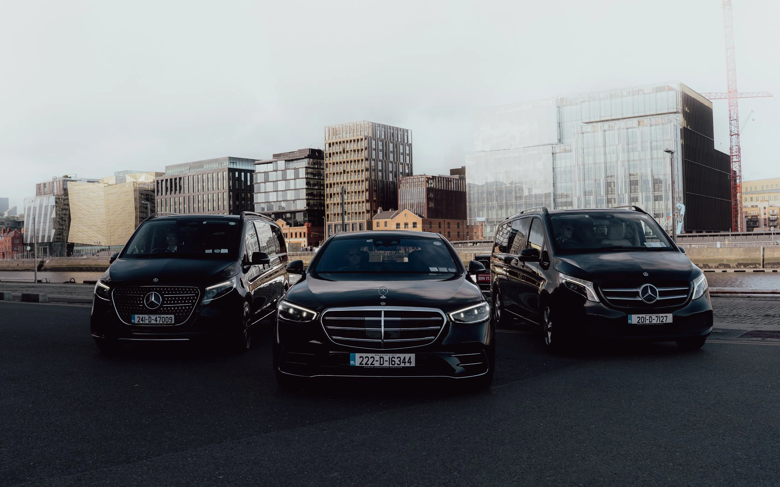 Three black Mercedes-Benz cars parked in front of modern city buildings.