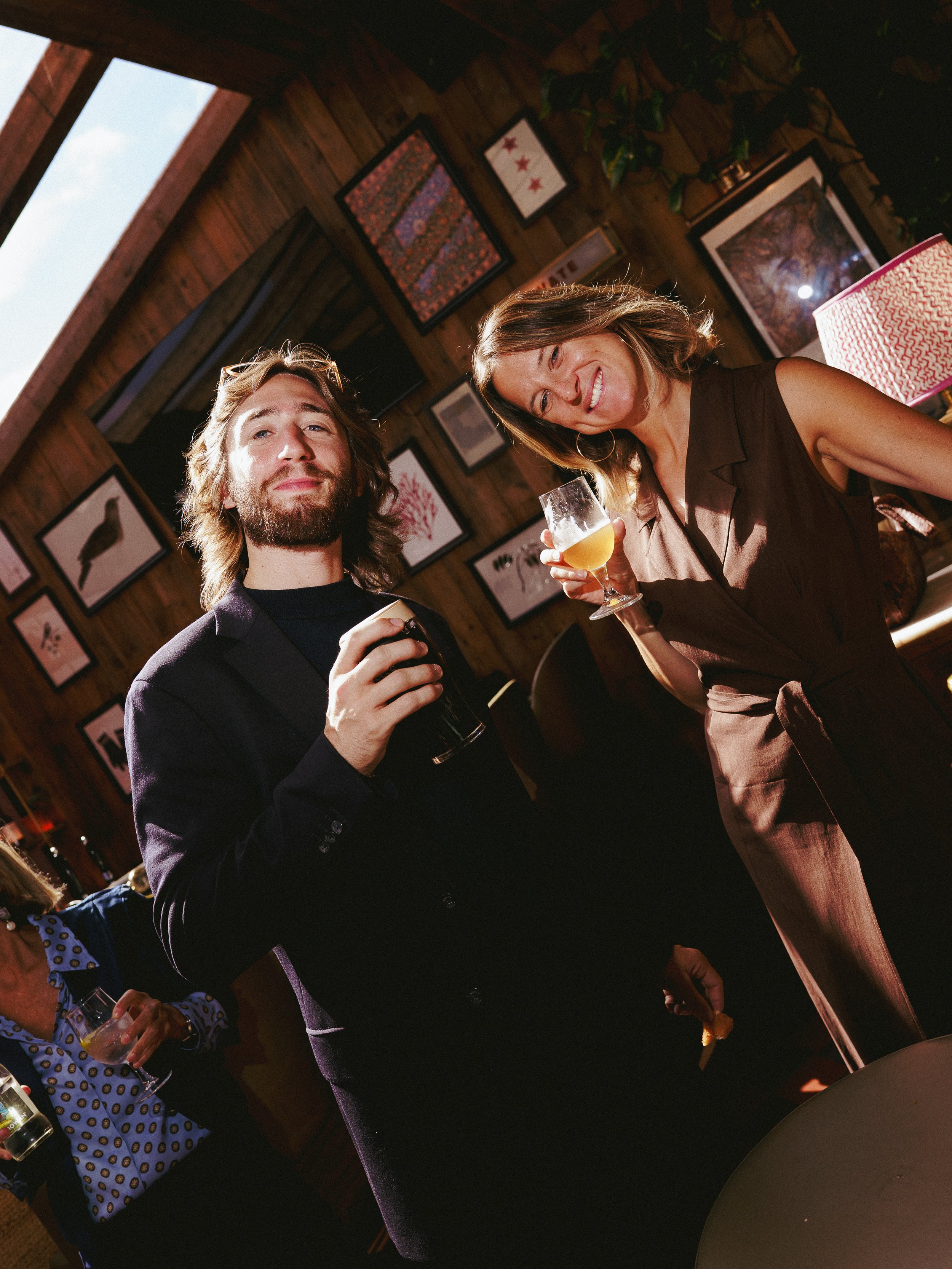 Two people smiling and raising glasses with drinks in a cozy, decorated indoor setting.
