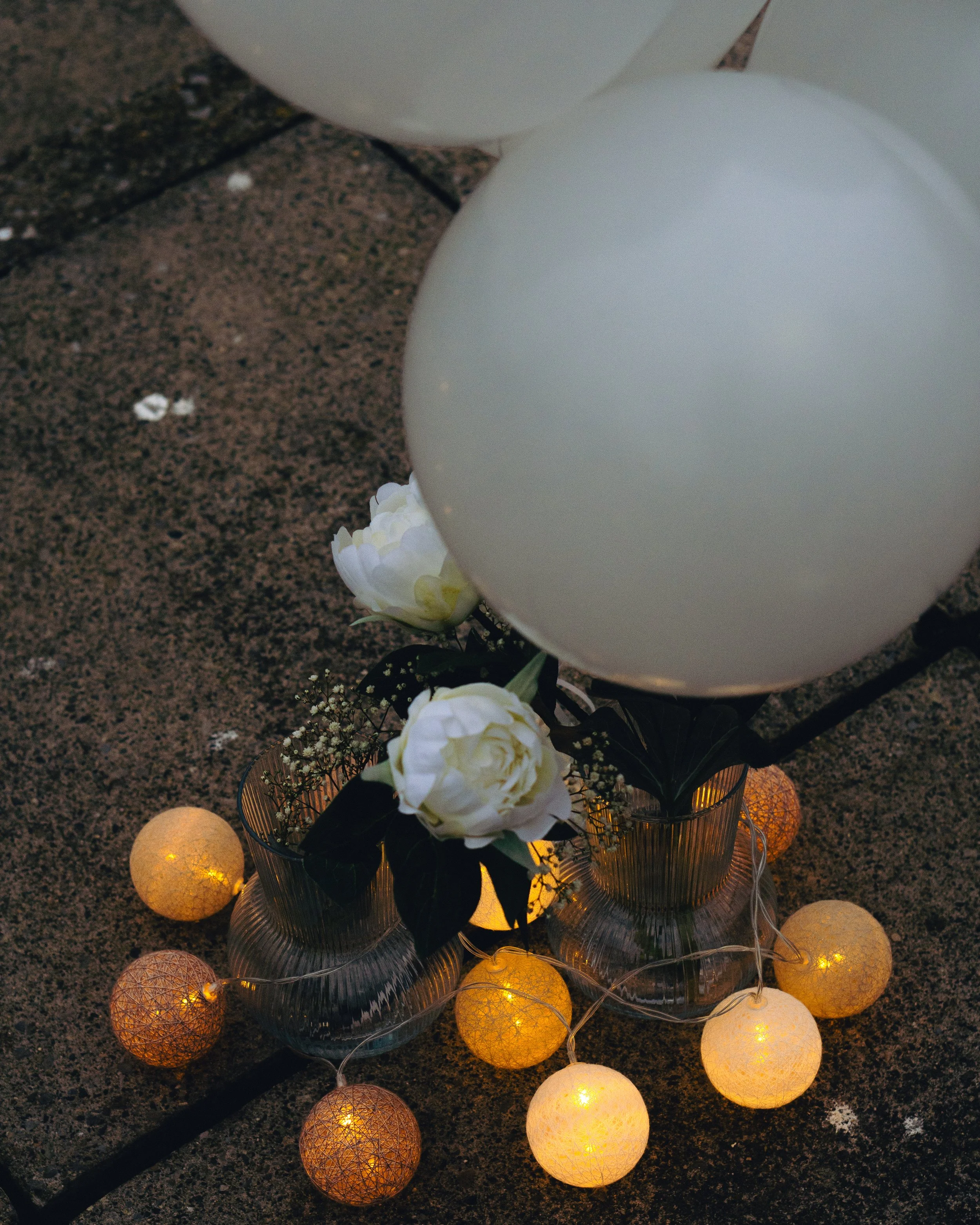 Flowers in glass vases surrounded by string lights on stone surface