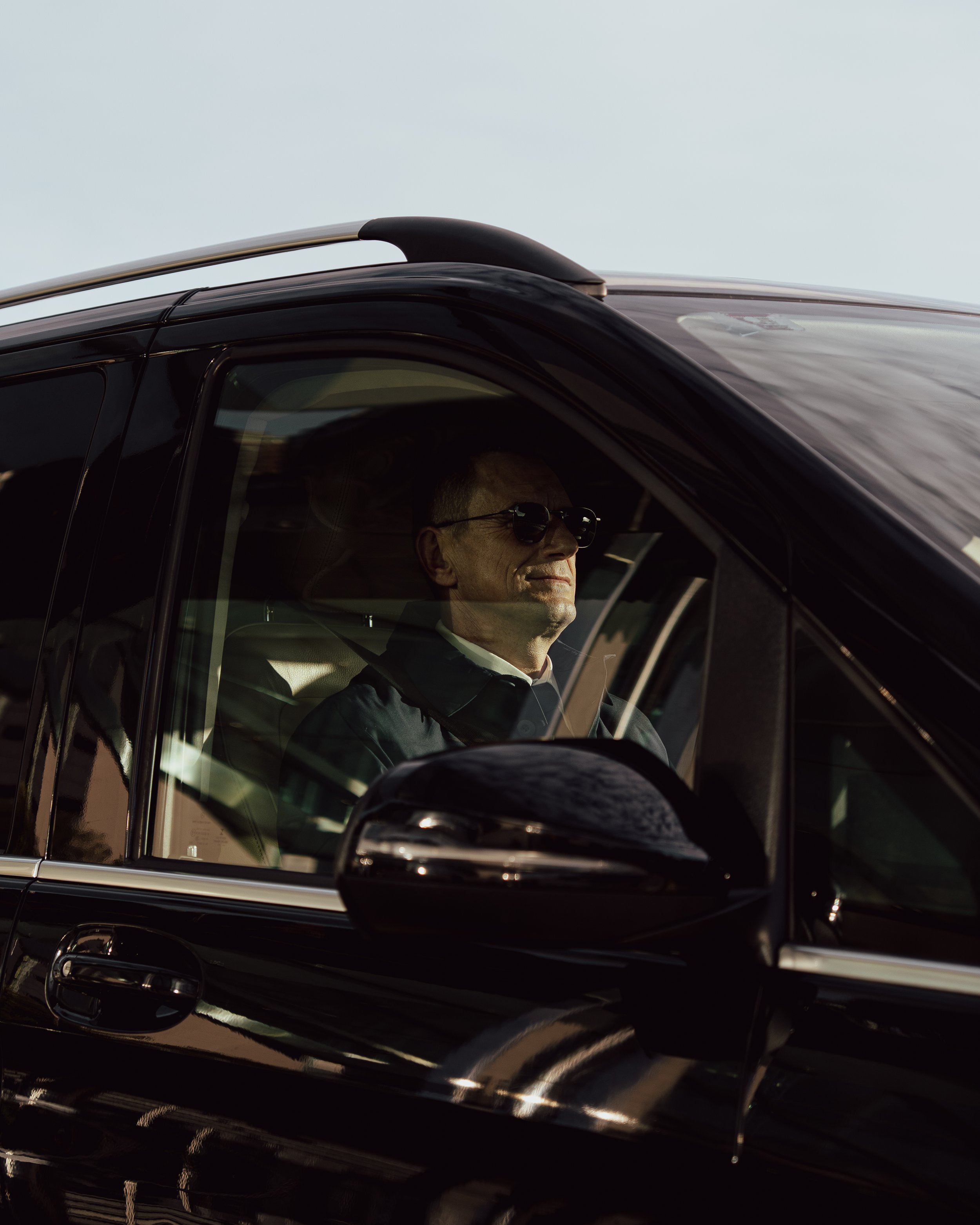 A man wearing sunglasses driving a black car.