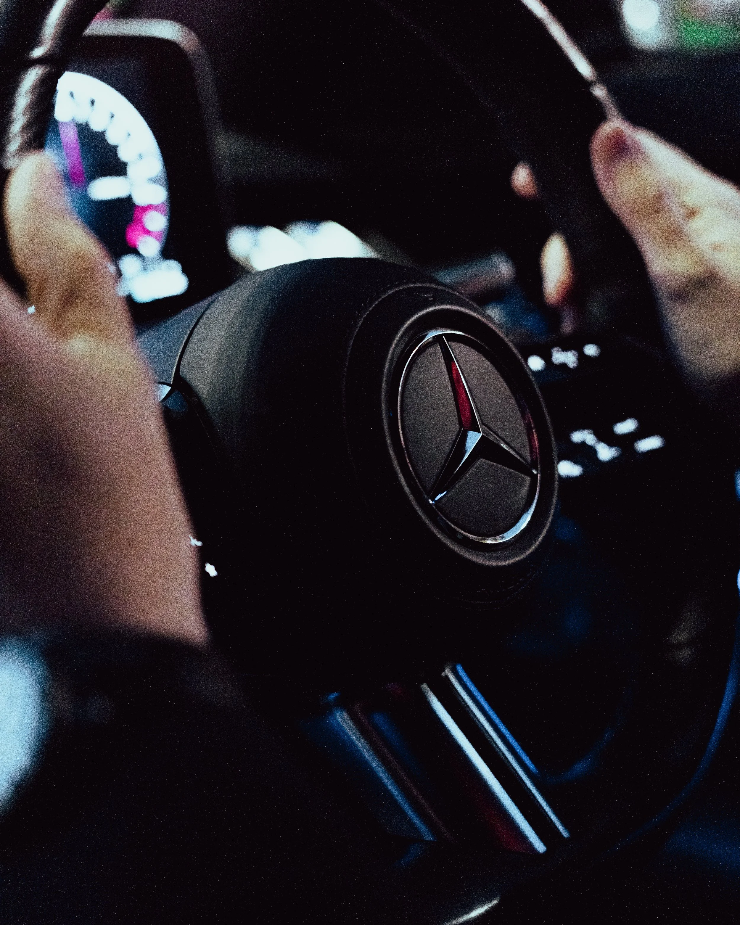 Close-up of a Mercedes-Benz steering wheel being held by someone inside a car, with the dashboard and instrument cluster visible in the background.