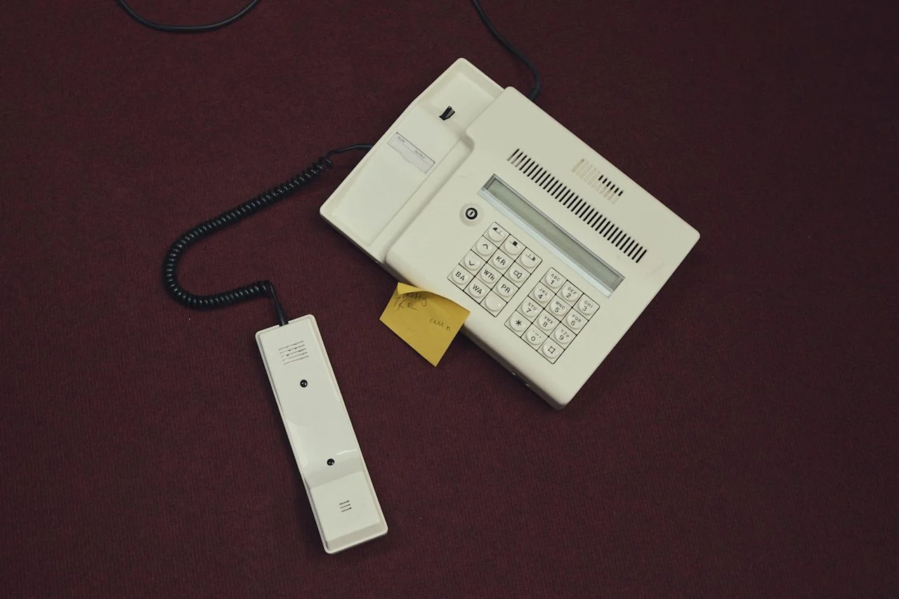 An office desk phone with a landline cord, a handset, a yellow sticky note, and a black background in an office for a small business in Winnipeg.