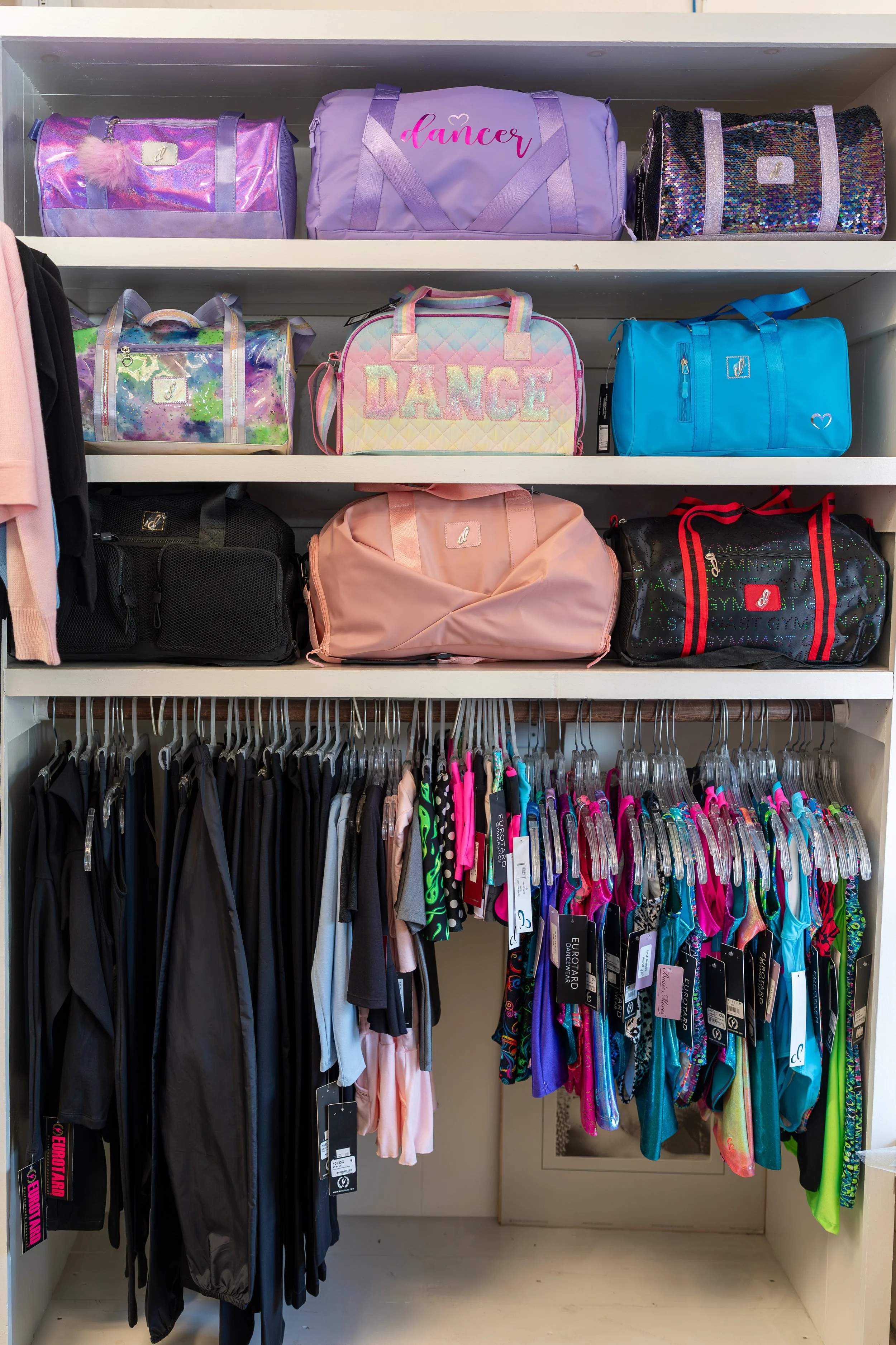 A closet with shelves filled with colorful gym bags and hanging athletic wear, including swimsuits and sports clothing.