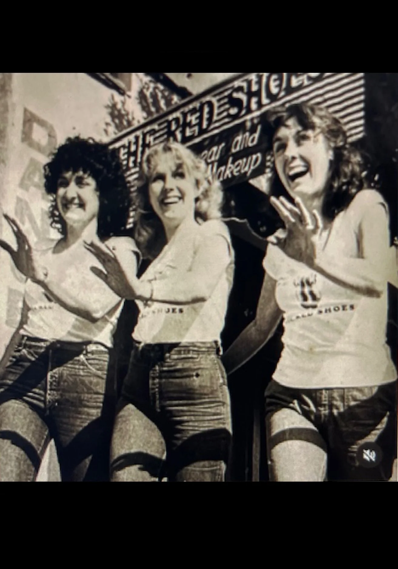 Three women standing in front of a sign, smiling and posing with arms crossed.