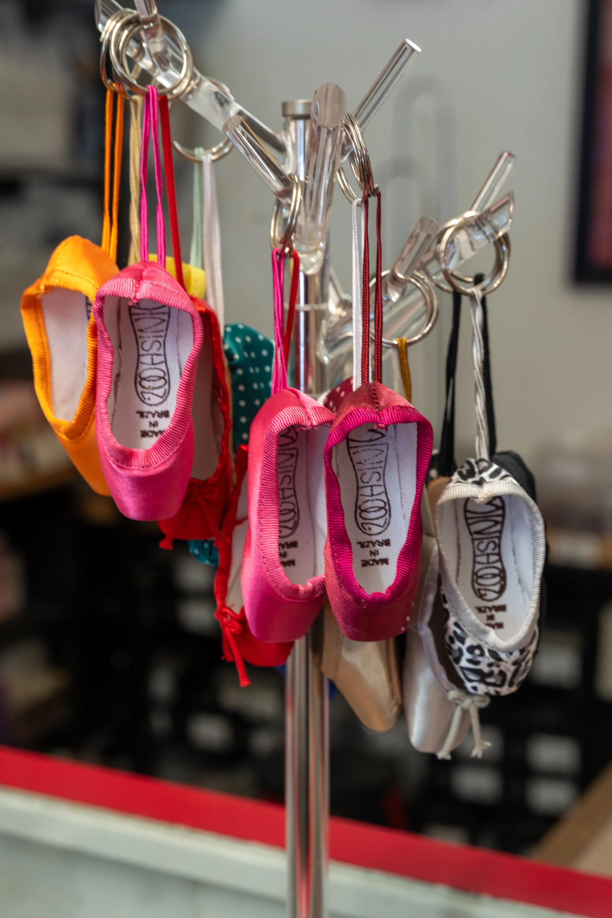 A metal stand holding small colorful socks with loops, including pink, orange, teal, beige, white with black patterns, and pink with darker pink, hanging on individual hooks.