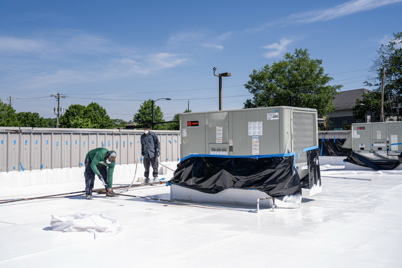 Two workers wearing masks spray foam insulation on a rooftop.