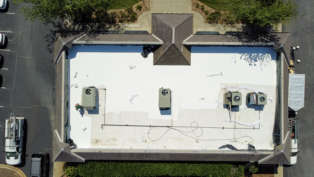 Aerial view of a building roof under construction with HVAC units, roofing materials, and workers present.