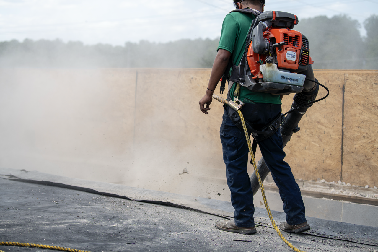 Worker using a backpack blower to clear debris or dust from a construction or roadwork site.