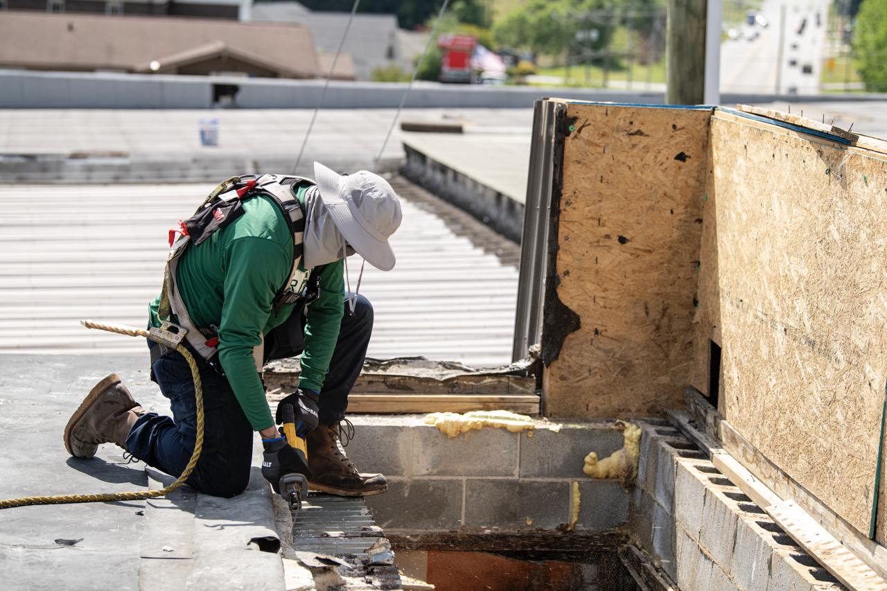 Construction worker kneeling on roof, cutting rebar while installing insulation and new roofing materials.
