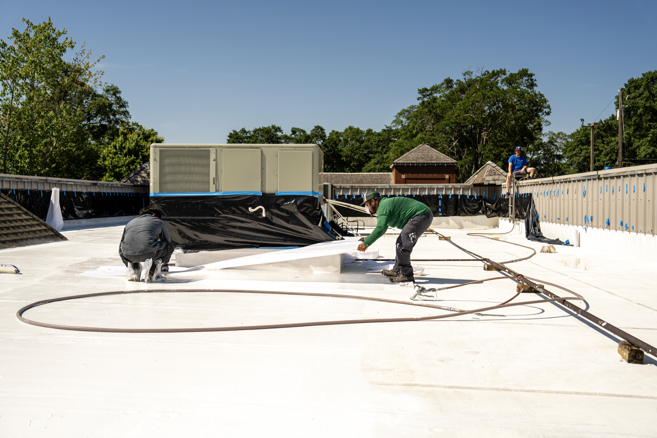 Workers applying a white coating to a building rooftop during construction under a clear blue sky.