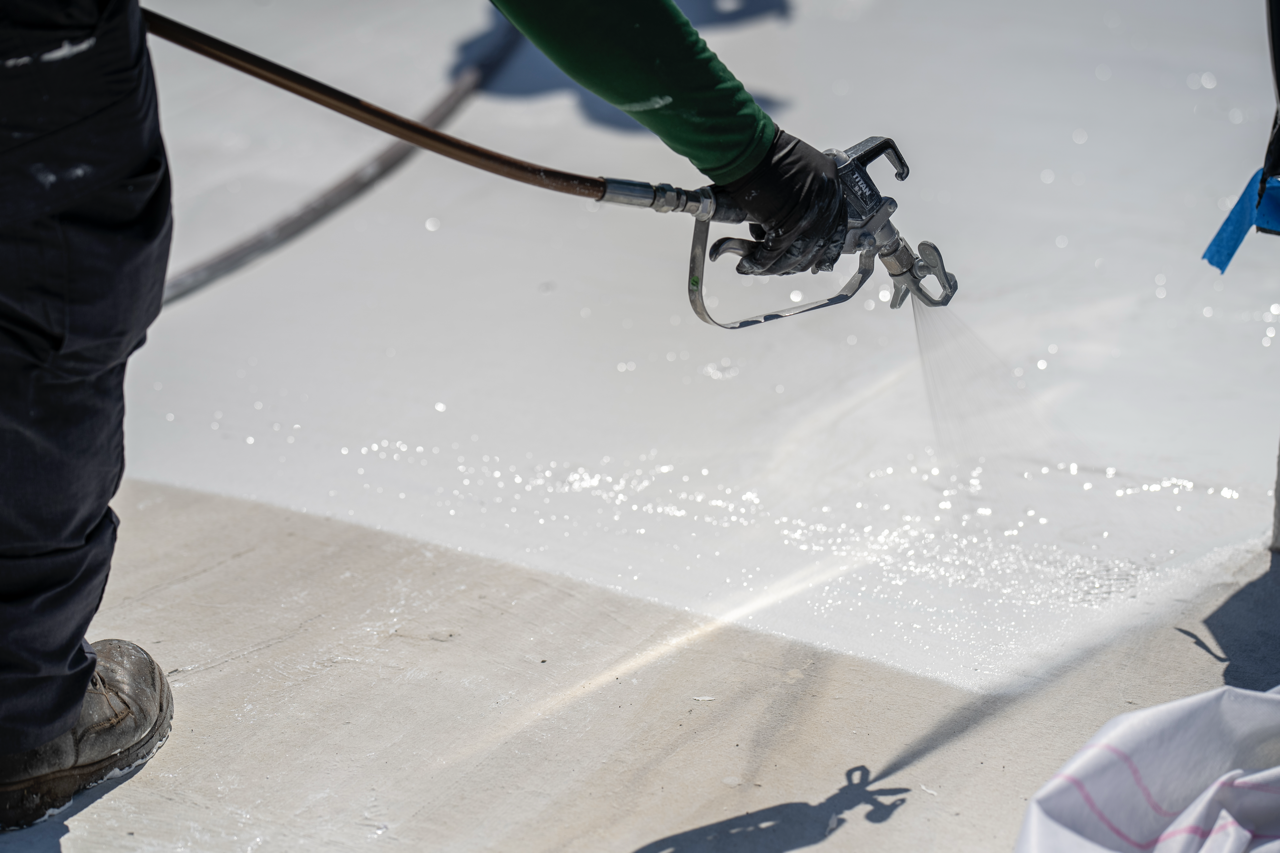 Person spray-painting a concrete surface with a sprayer, water or paint visible in the spray nozzle