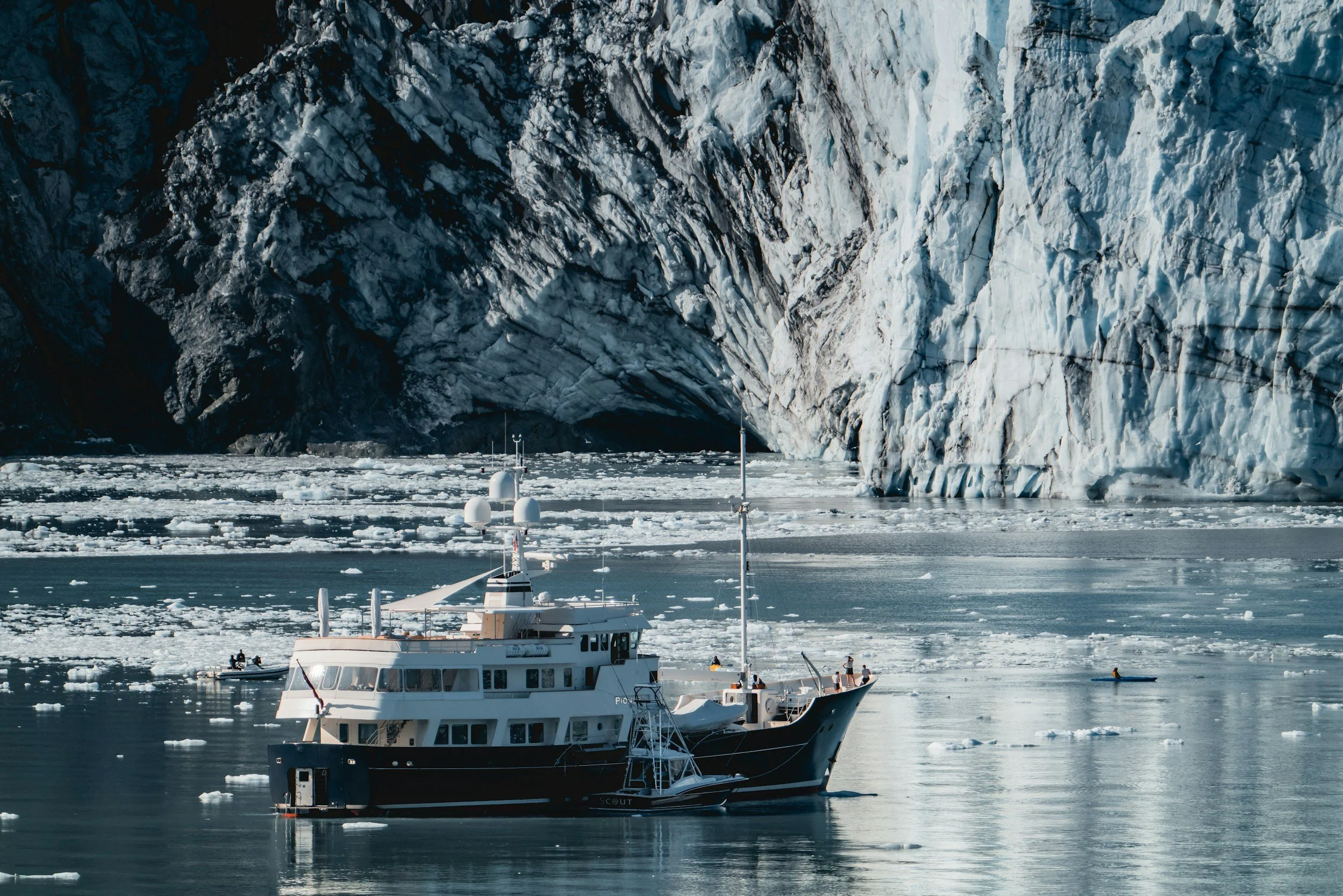 A boat sailing in icy waters near a large snow-covered glacier face with ice floating on the water.