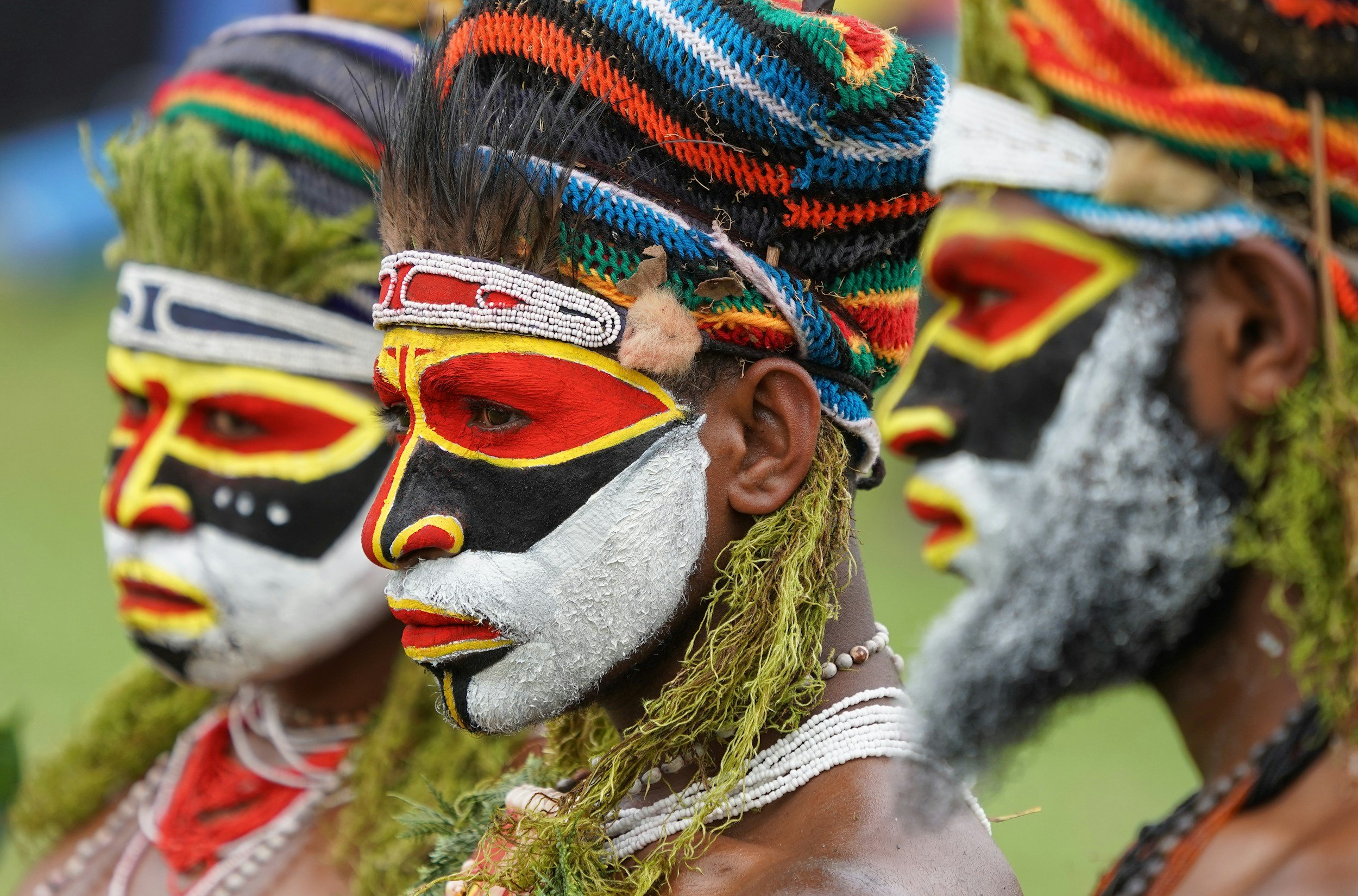 Close-up of multiple indigenous individuals with face paint and traditional headdresses, standing in a line outdoors.