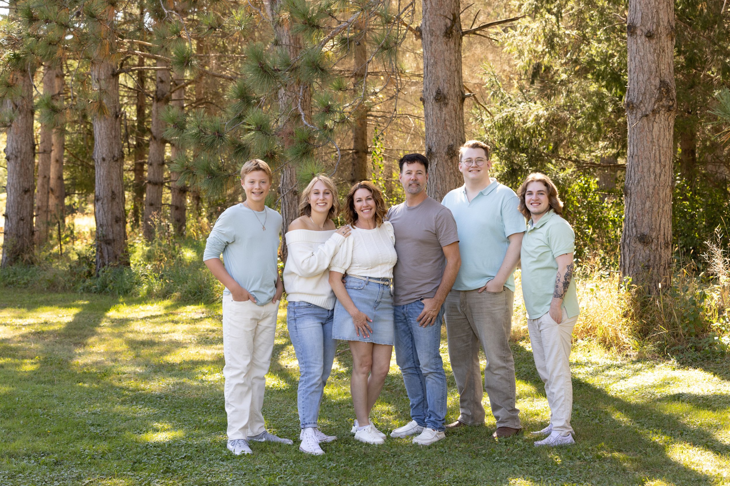 Family of seven standing outdoors in a forest, smiling at the camera, during daytime.