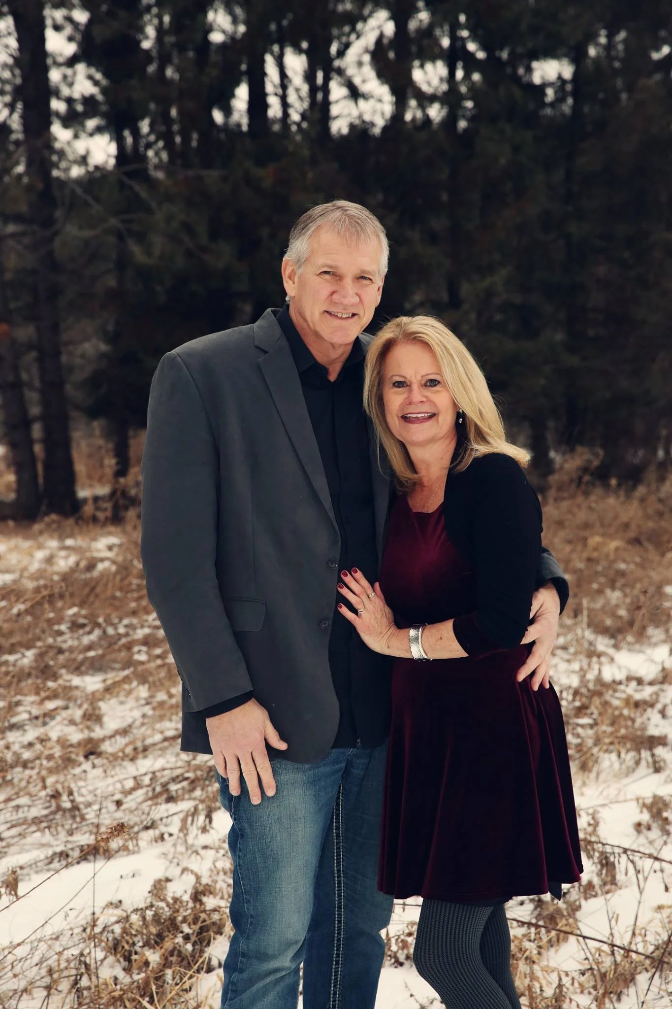 A man and woman standing close together outdoors in a snowy field with trees in the background, smiling at the camera.