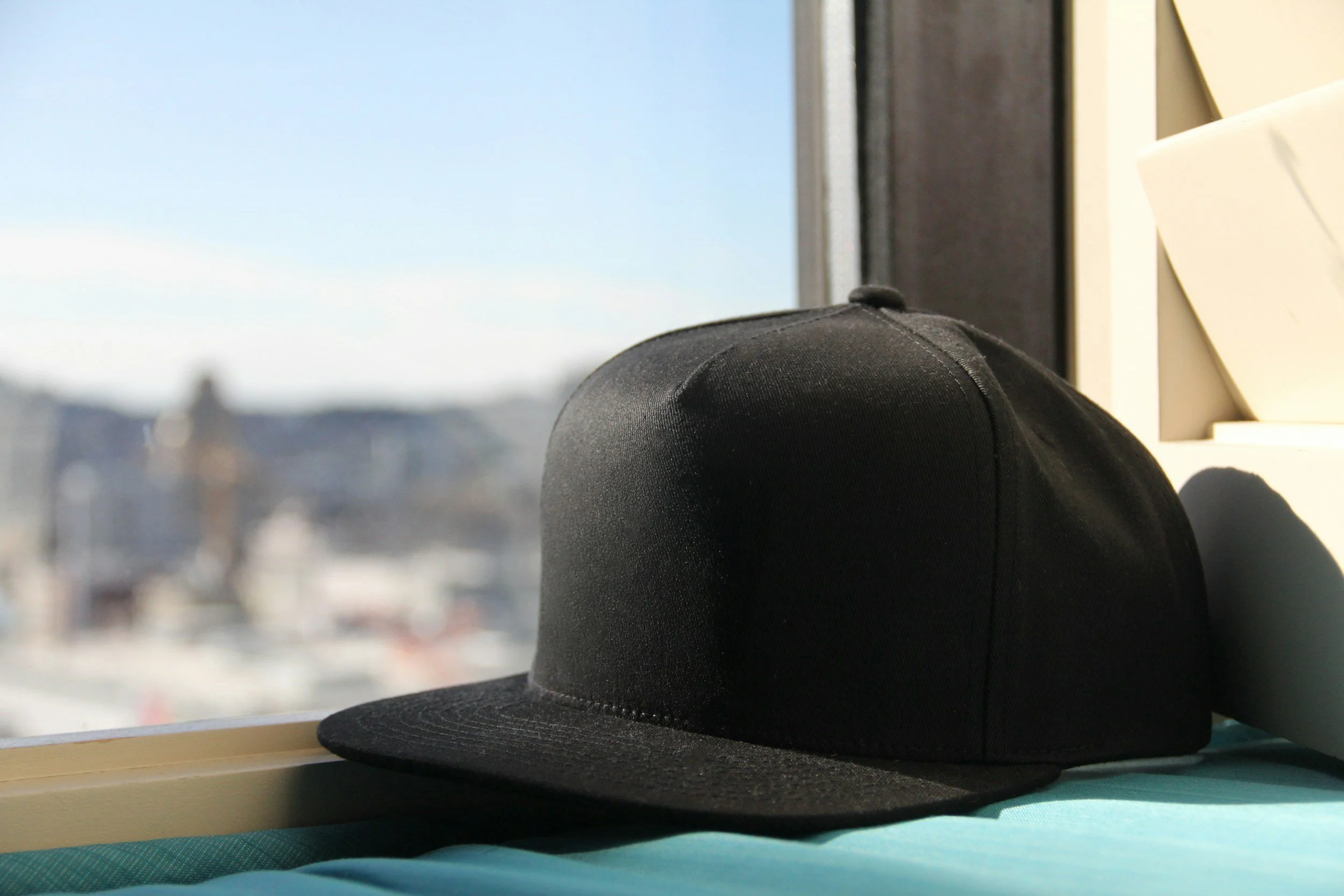 Black cap resting on a windowsill with a blurred cityscape in the background.