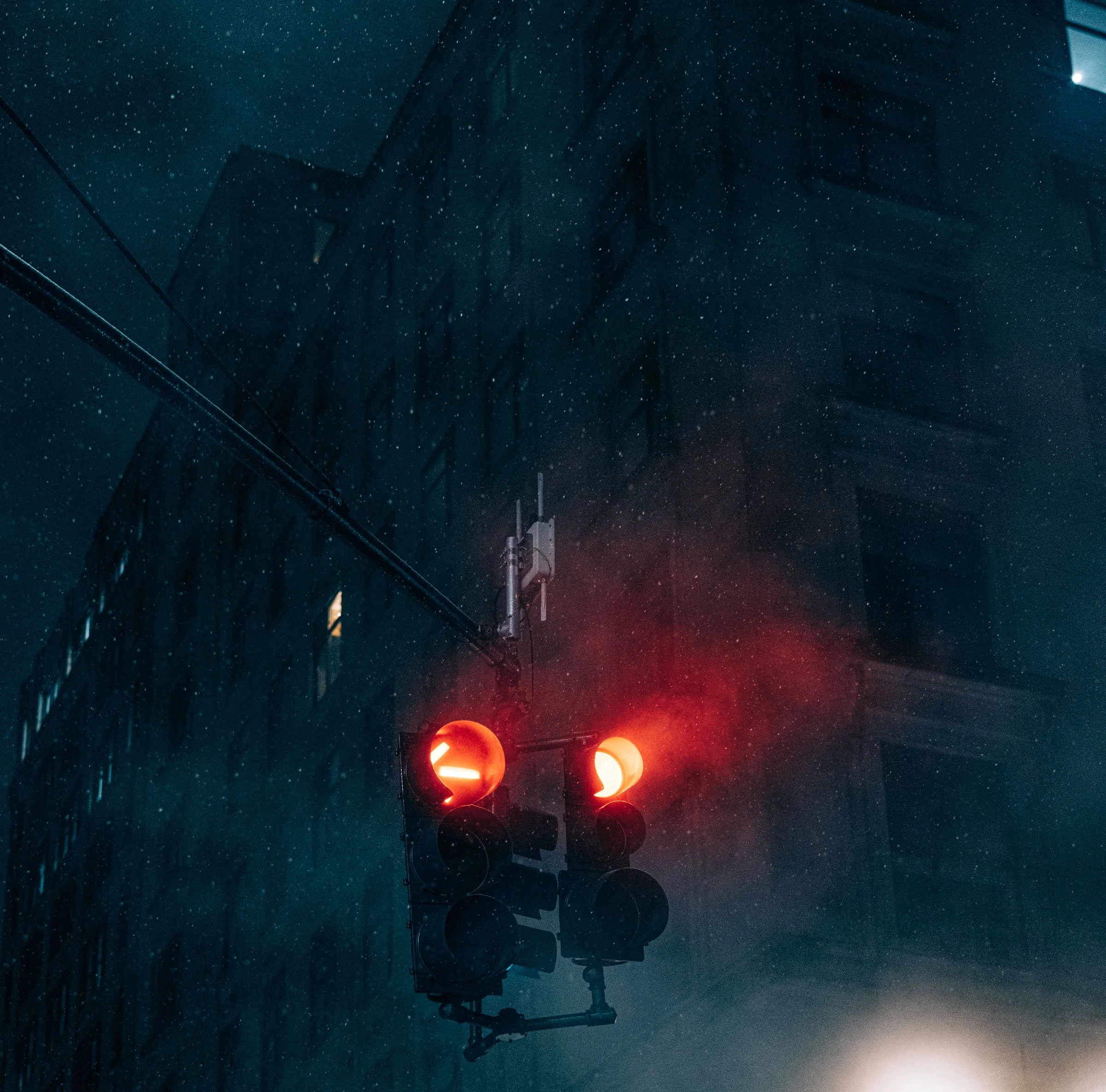 Two red traffic signals glowing through heavy falling snow at night beside a dark building, Midtown Manhattan, New York.