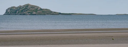 A green headland rising across the water beyond the wide sands of Portmarnock beach, Dublin, at low tide.