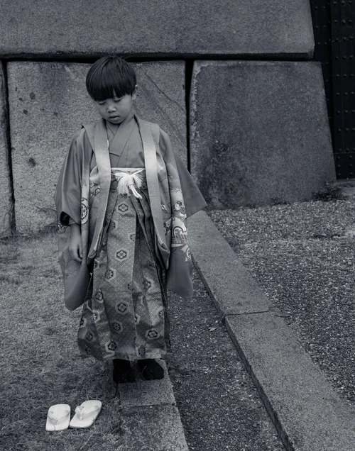 A child in a kimono walking down a stepped alley, head bowed, Osaka, in black and white.