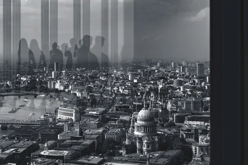 Black and white double exposure of an aerial view of London, with St Paul's Cathedral and the River Thames, overlaid with the reflected silhouettes of people gathered at a high viewing gallery.