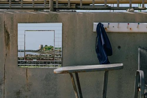 A blue coat hanging on a peg in a weathered concrete bathing shelter at Howth, Dublin, the sea visible through the opening beyond.