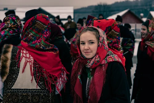 A young woman in a red floral headscarf and traditional dress among others at a winter gathering, Bucovina, Romania.
