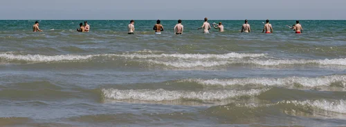 People wading in the shallow sea off Portmarnock beach, Dublin, a wide flat shoreline under a grey sky.