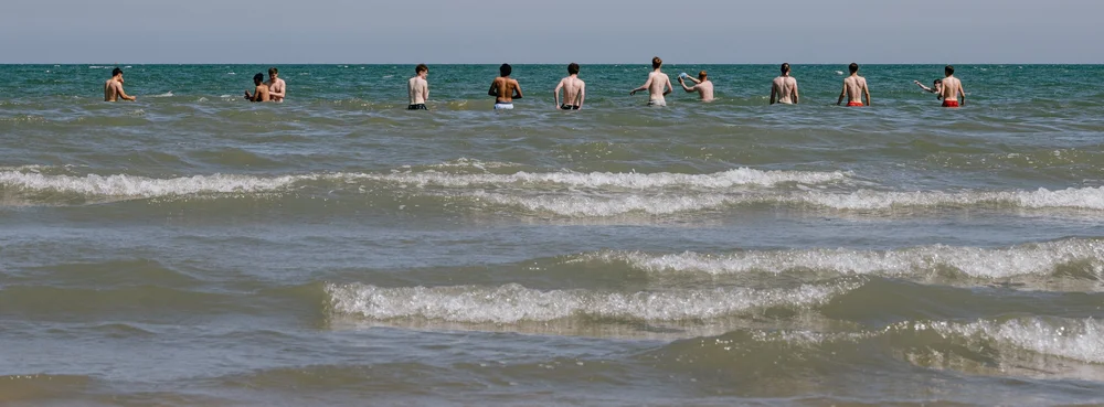 People wading in the shallow sea off Portmarnock beach, Dublin, a wide flat shoreline under a grey sky.