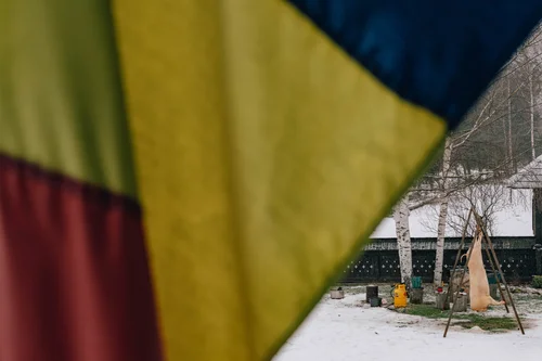 A Romanian tricolour flag in the foreground against a snowy village scene, a conical haystack beyond, Bucovina, Romania.