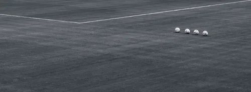 Black and white photo of four footballs lined up in a row on an empty grass pitch near a white boundary line
