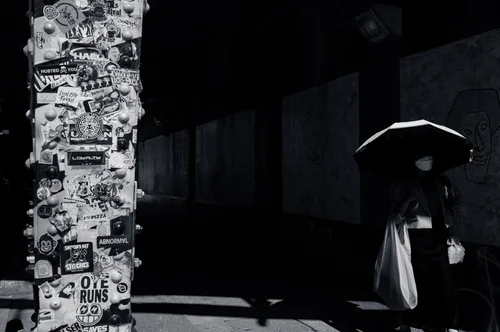 A figure with an umbrella passing a wall of posters at night, Tokyo, in black and white.