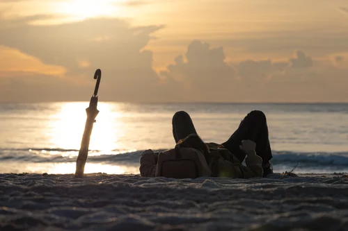 A person reclining on the sand at the water's edge at sunrise, a post beside them, golden light across the sea, Miami Beach.