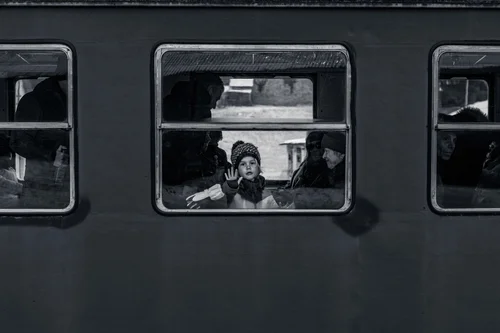 A child pressing a hand to the window of a dark train carriage, faces looking out from within, Bucovina, Romania, in black and white.