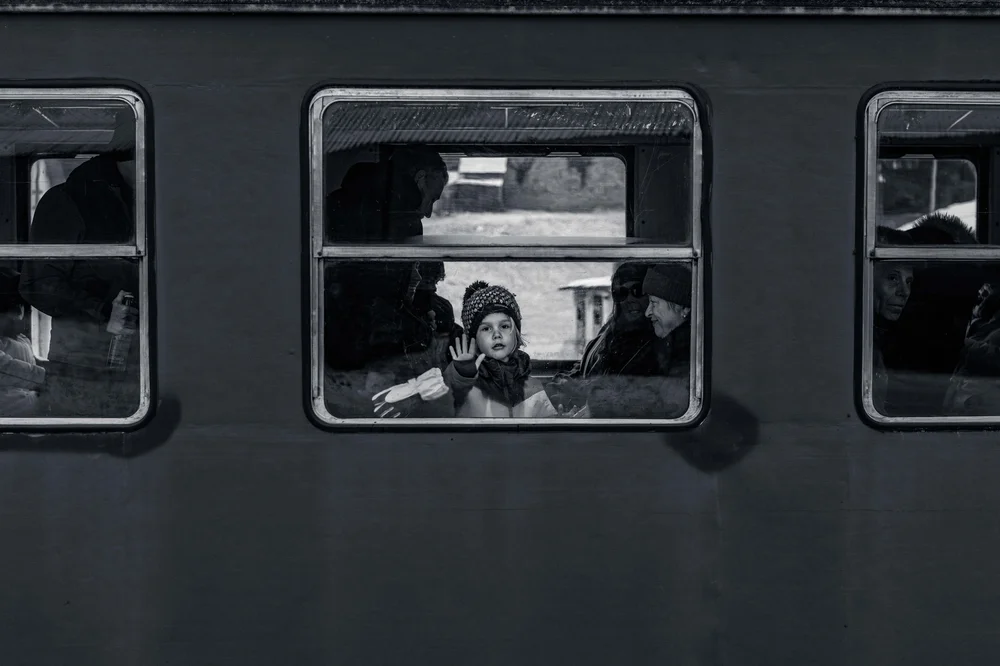 A child pressing a hand to the window of a dark train carriage, faces looking out from within, Bucovina, Romania, in black and white.