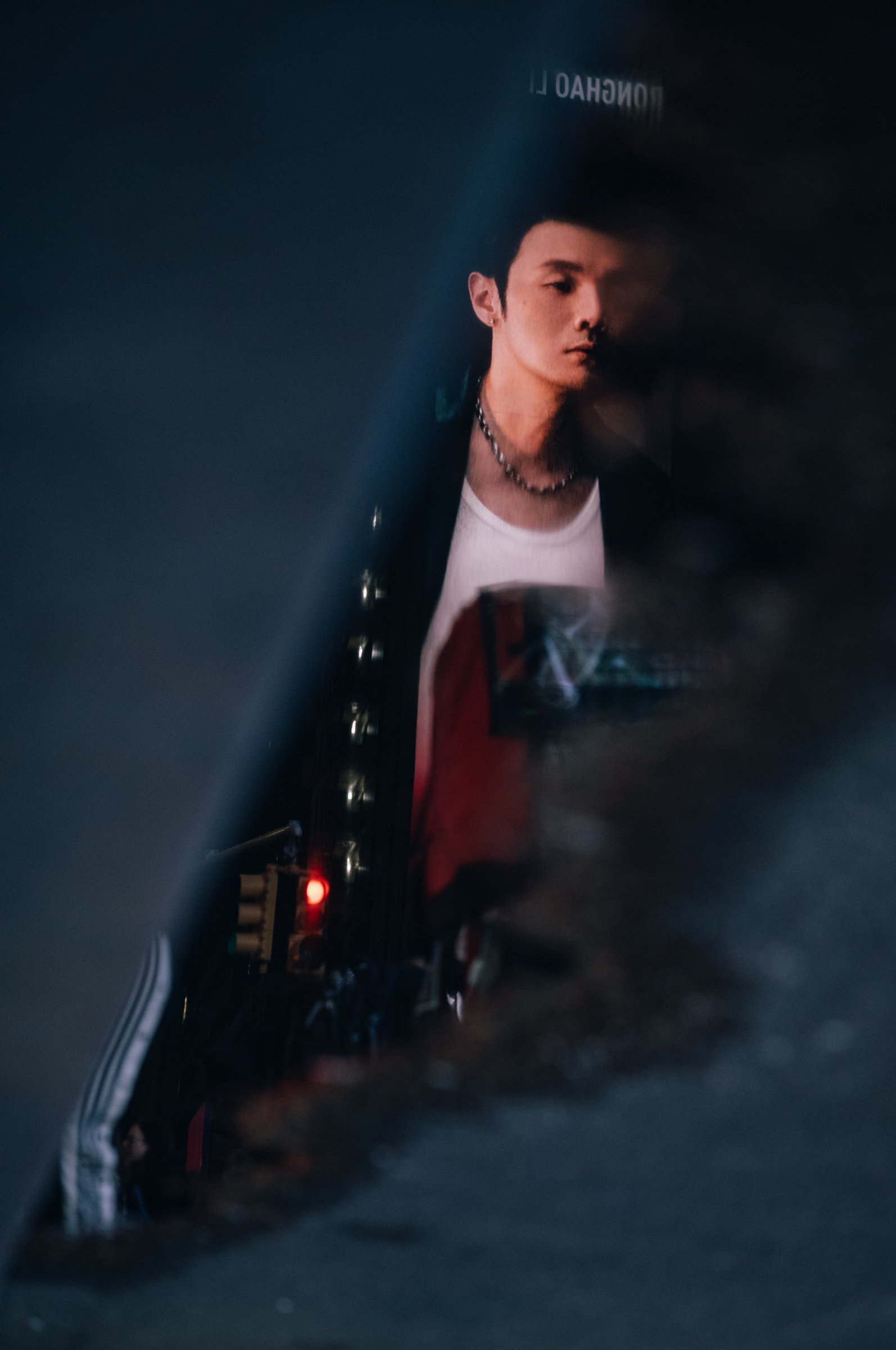 A reflection of a Times Square advertising board caught in a sliver of wet ground, a man's face and a red banner appearing between the dark edges of the street, New York.